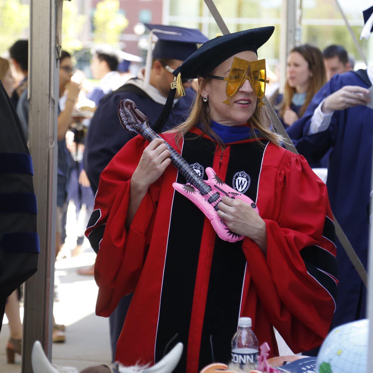 A picture of a woman in graduation regalia holding a pink inflatable guitar. 